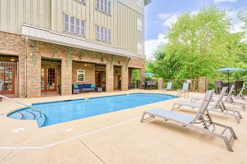 a pool with chaise lounge chairs and umbrellas at the enclave at woodbridge apartments